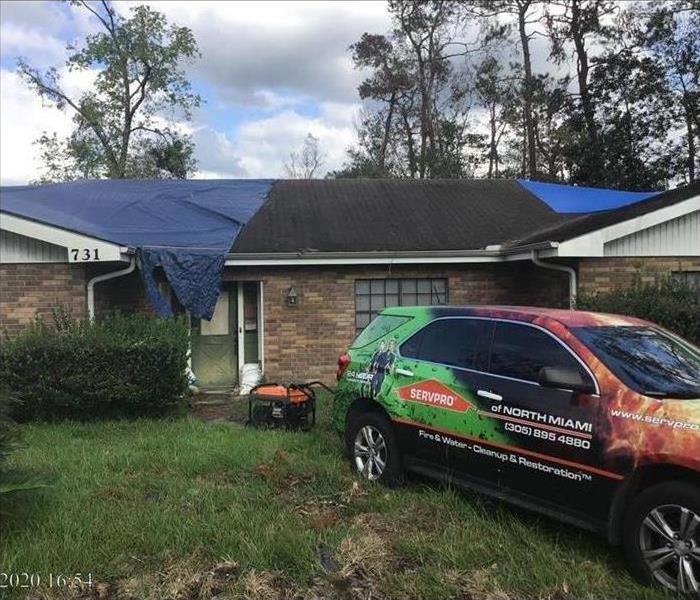 Servpro vehicle parked in front of a house, roof of the house has a blue tarp